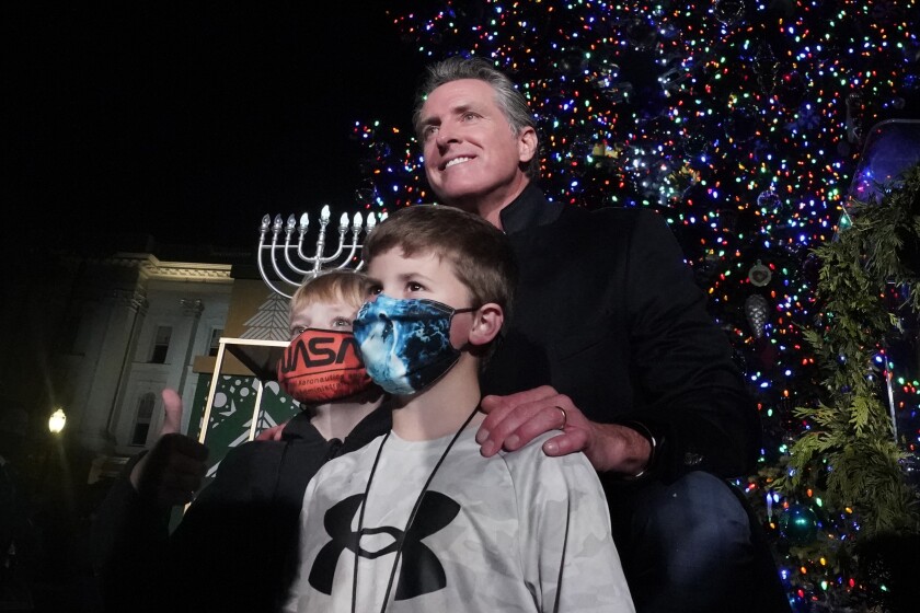 California Gov. Gavin Newsom poses for a photo with a pair of youngsters after the 90th annual State Capitol Tree Lighting Ceremony in Sacramento, Calif., Thursday, Dec. 2, 2021. Newsom has written a children's book inspired by his experiences dealing with dyslexia as a kid. The book, titled "Ben & Emma's big Hit," co-authored by Ruby Shamir, with illustrations by Alexandra Thompson, tells the story of a young boy who, with the help of a caring teacher and a friend uses baseball to cope with his dyslexia. The book is published by Philomel books and comes out Tuesday, Dec. 7. (AP Photo/Rich Pedroncelli)