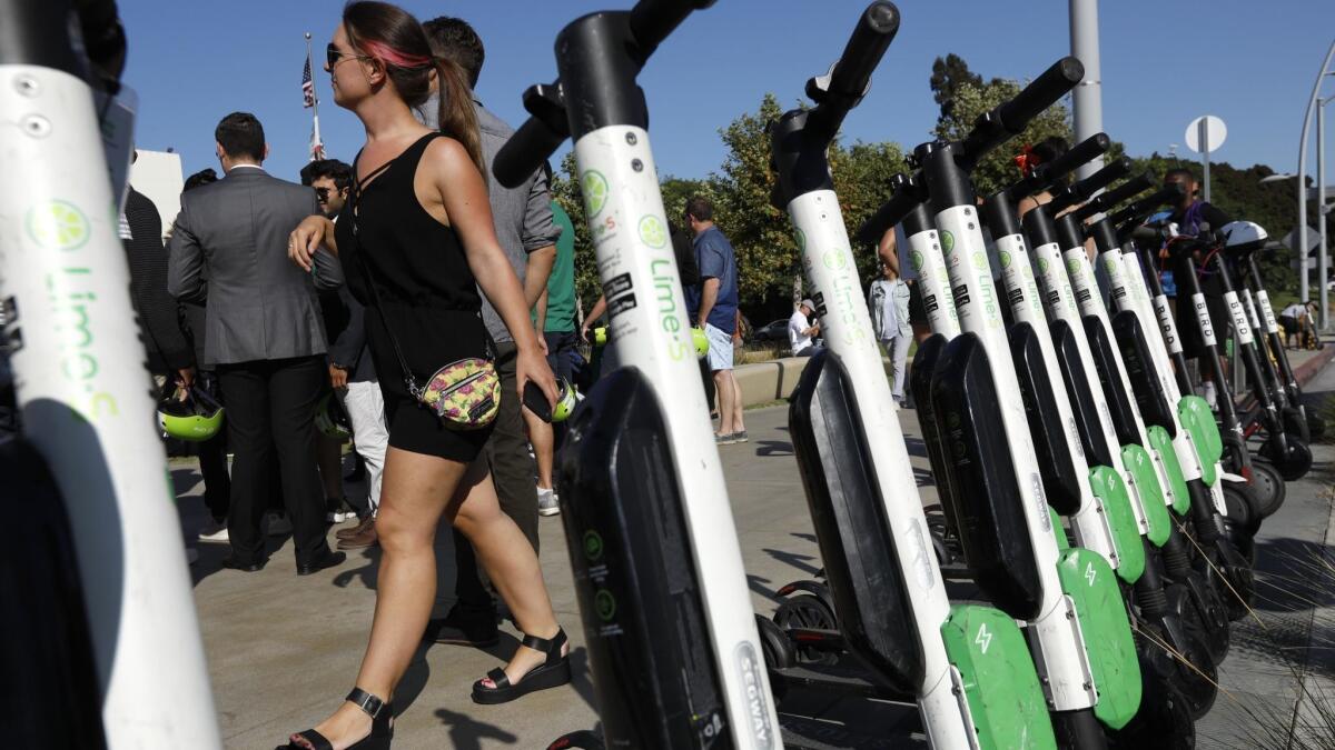 A pedestrian walks past a row of parked Lime and Bird scooters near Santa Monica City Hall in August.