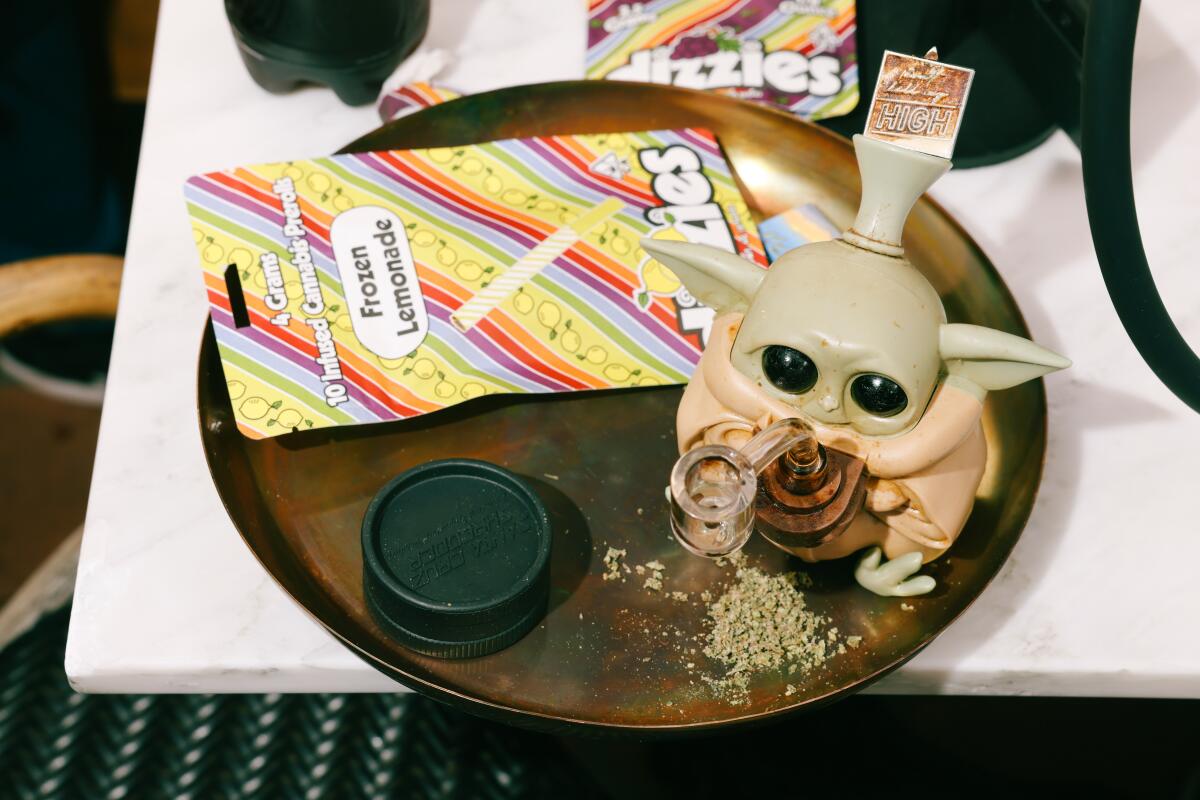 A tray with a Baby Yoda-shaped pipe, loose cannabis flower and a striped envelope.