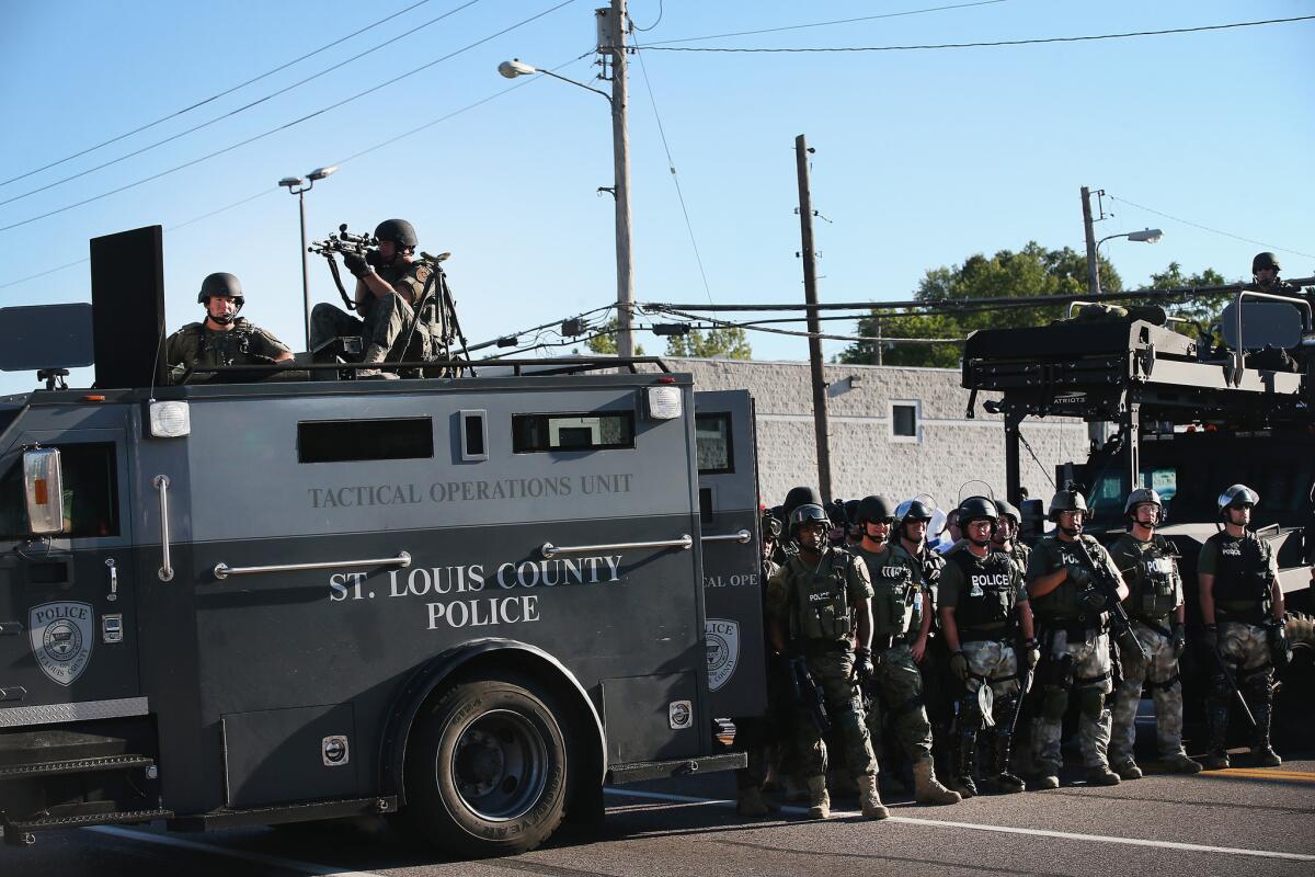 Police in riot gear stand with armored vehicle watching protesters in Ferguson, Mo., on Aug. 13.