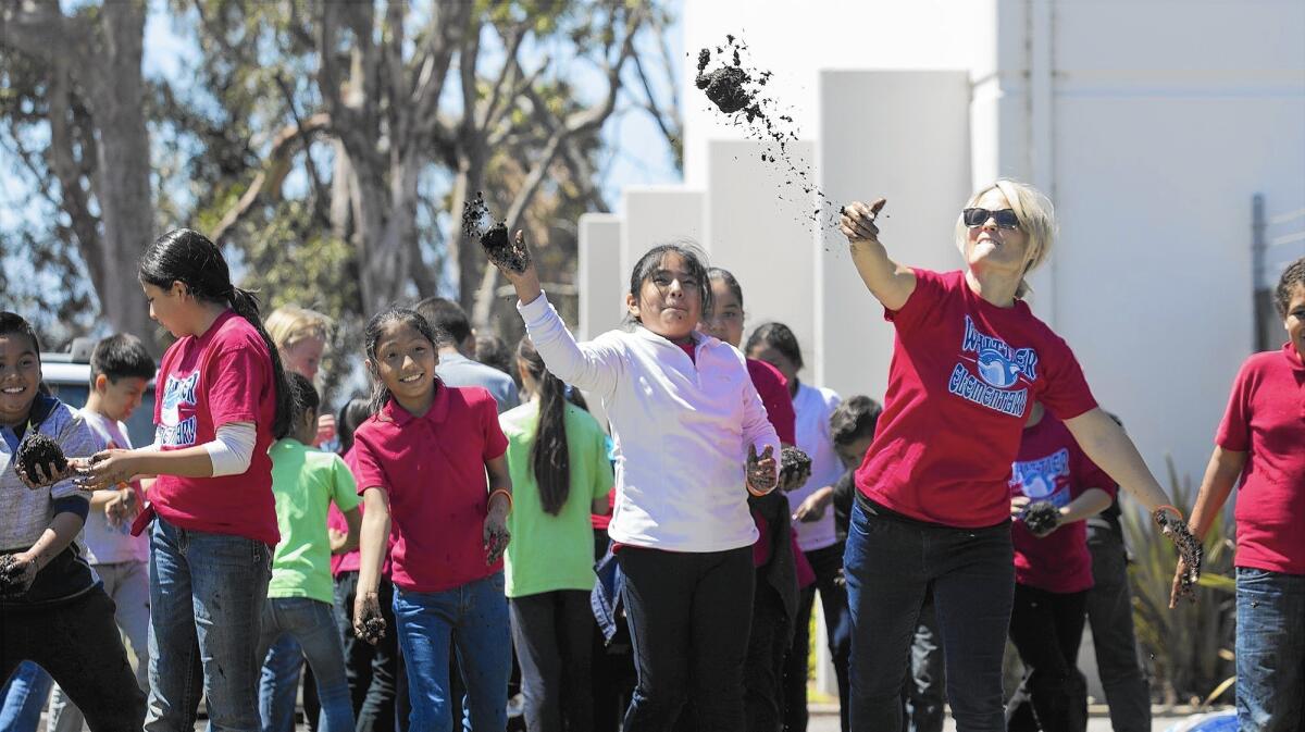 Whittier Elementary School fourth grade teacher Melissa Guerin, right, throws a mud ball with her students during an Earth Day celebration at Newport Banning Land Trust in Costa Mesa on Tuesday.