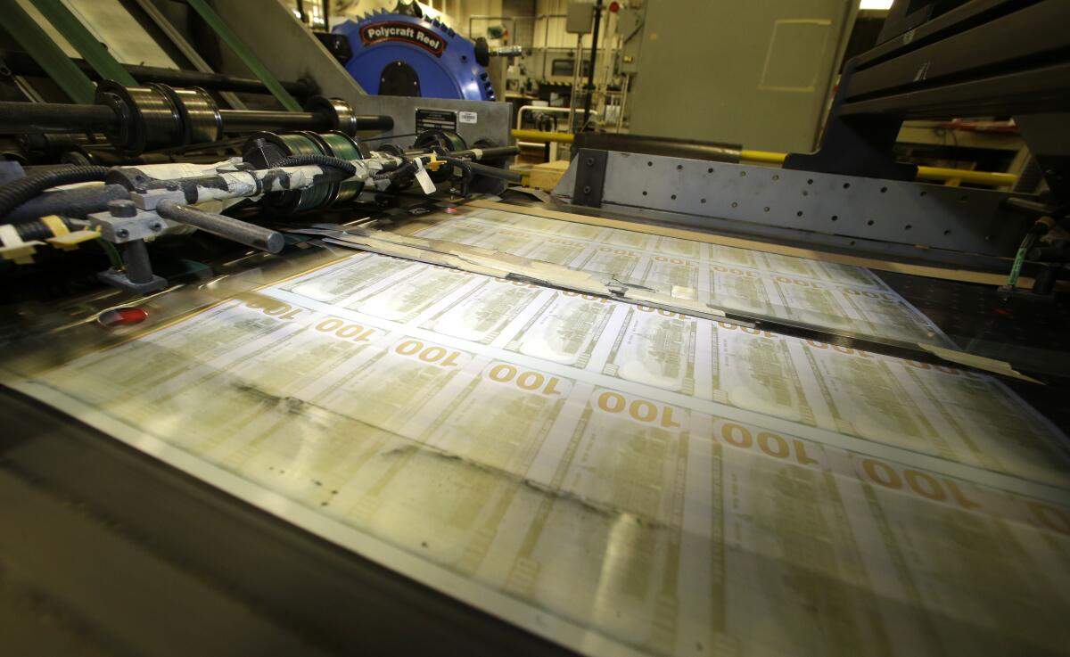 Sheets of uncut $100 bills run through a printing press.