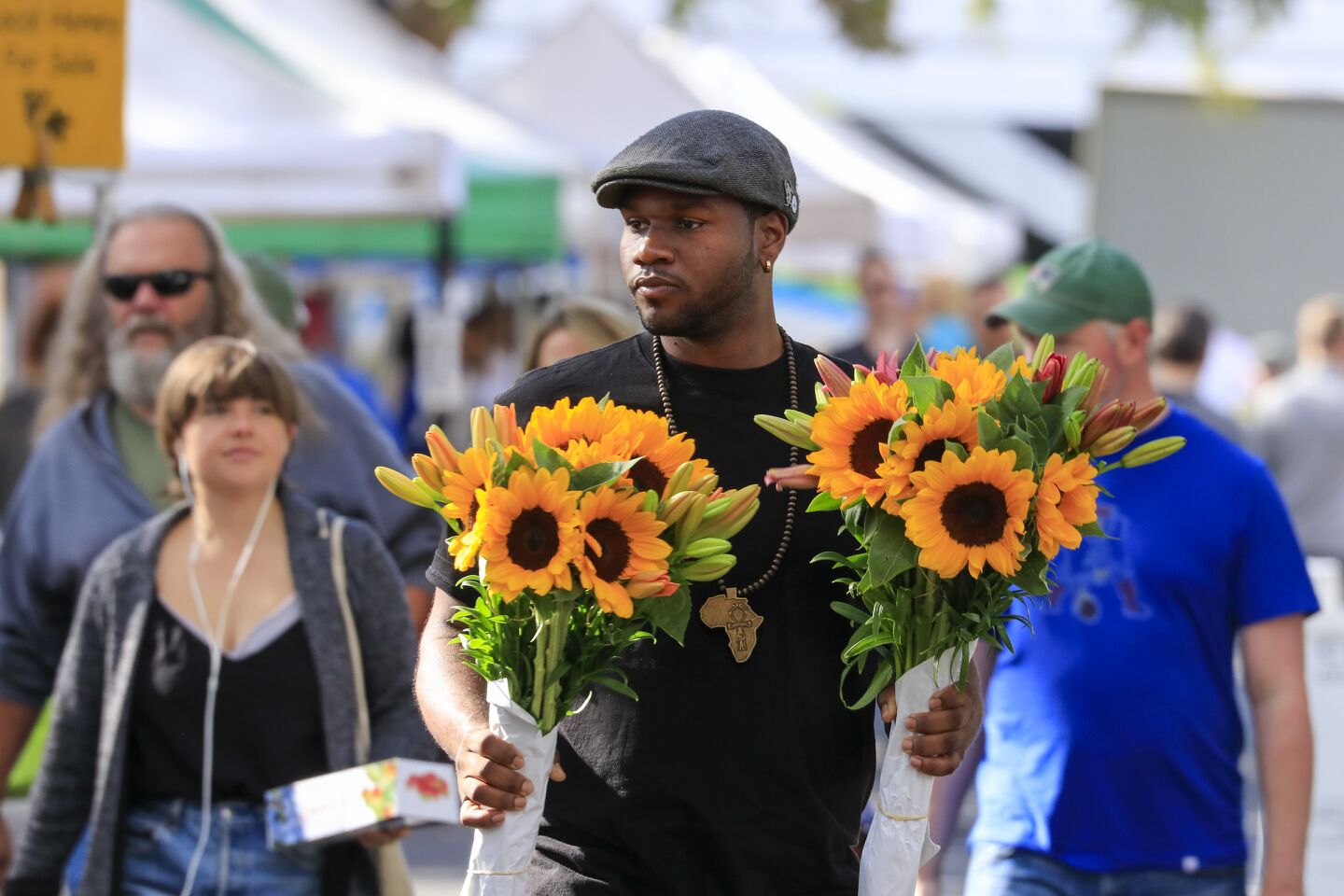 Customer Steven Russell carries two sunflower bouquets through the Claremont Farmers & Artisans Market in the heart of the Claremont Village in the city of Claremont.