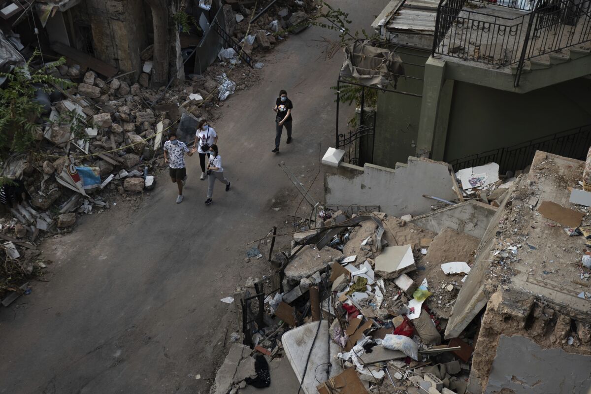 People walk next debris from destroyed buildings on a neighborhood near the site of last week's explosion that hit the seaport of Beirut, Lebanon, Thursday, Aug. 13, 2020. (AP Photo/Felipe Dana)