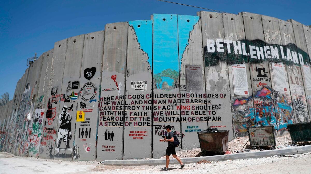 A tourist walks past new graffiti painted on Israel's controversial separation barrier in the West Bank city of Bethlehem, on May 15.