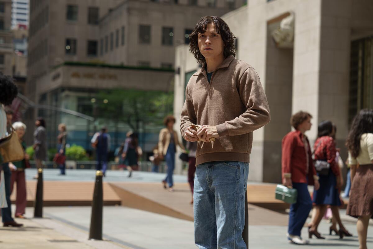 A long-haired Tom Holland stands on a city street.