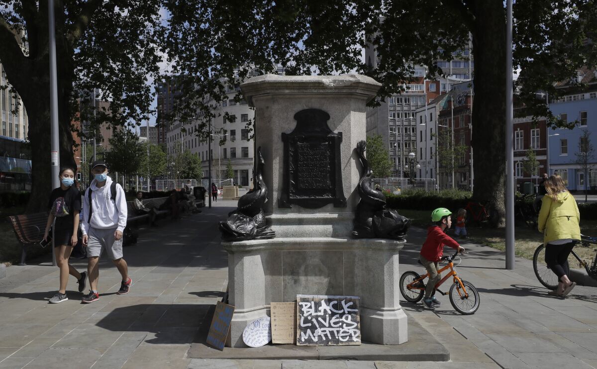 FILE - People walk past the empty plinth after a statue of Edward Colston was pulled down during a Black Lives Matter demo, in Bristol, England, June 8, 2020. A 311-year-old school in southwest England named after the slave trader Edward Colston is to change its name following a wide-ranging consultation. The governors of the fee-paying Colston’s School, which was set up in 1710 in Bristol, said Monday, Dec. 6, 2021 that the school will be renamed next summer with current and former students, parents and staff all to have a say.(AP Photo/Kirsty Wigglesworth, file)