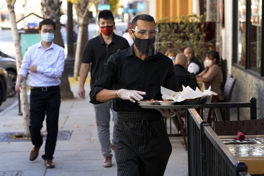 FILE - A waiter wears a mask and face covering at a restaurant with outdoor seating Tuesday, Dec. 1, 2020, in Pasadena, Calif. The U.S. services sector, where most Americans work, registered its sixth consecutive month of expansion in November. The Institute for Supply Management reported Thursday that its index of services activity declined slightly to a reading of 55.9 last month, from a reading of 56.6 in October. (AP Photo/Marcio Jose Sanchez, File)
