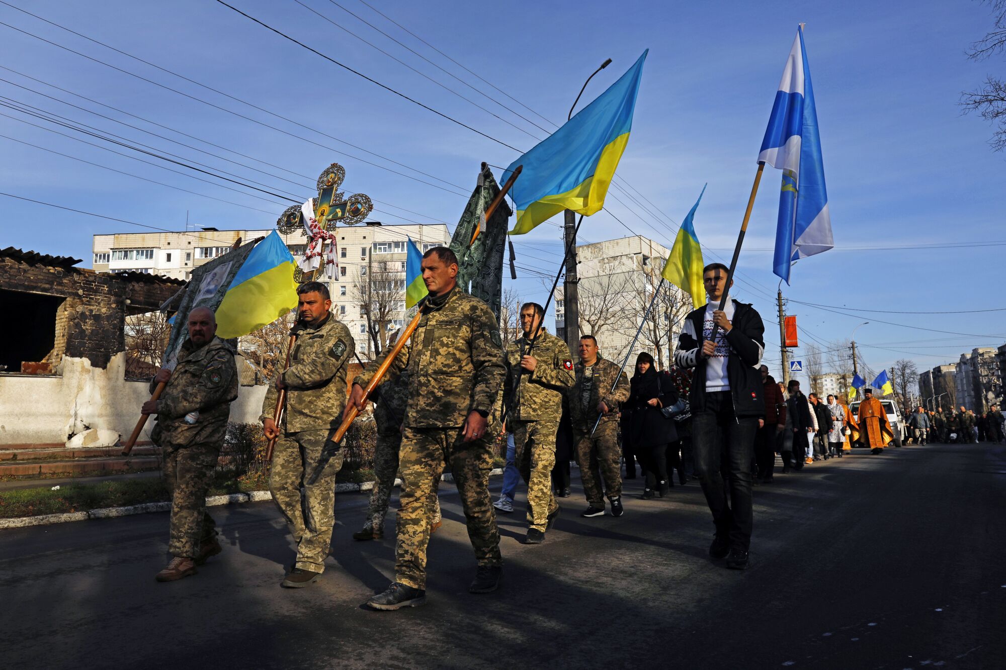 Men in uniform carry blue-and-yellow Ukrainian flags on a street 