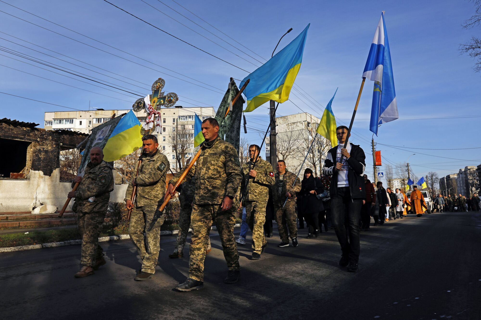 Men in uniform carry blue and yellow Ukrainian flags down the street. 