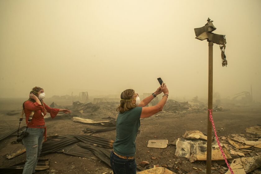 GREENVILLE, CA - AUGUST 07, 2021: Kelly Tan, 59, left, looks on as her sister, Tiffany Lozano, 44, photographs melted street signs on Main St. in Greenville, caused by the extreme temperature of the Dixie Fire that destroyed most of the town. Lozano is a resident of nearby Quincy and Tan is a resident of nearby Taylorsville. (Mel Melcon / Los Angeles Times)
