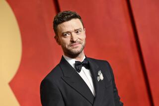 Justin Timberlake wears a black tuxedo while posing in front of a yellow and red backdrop