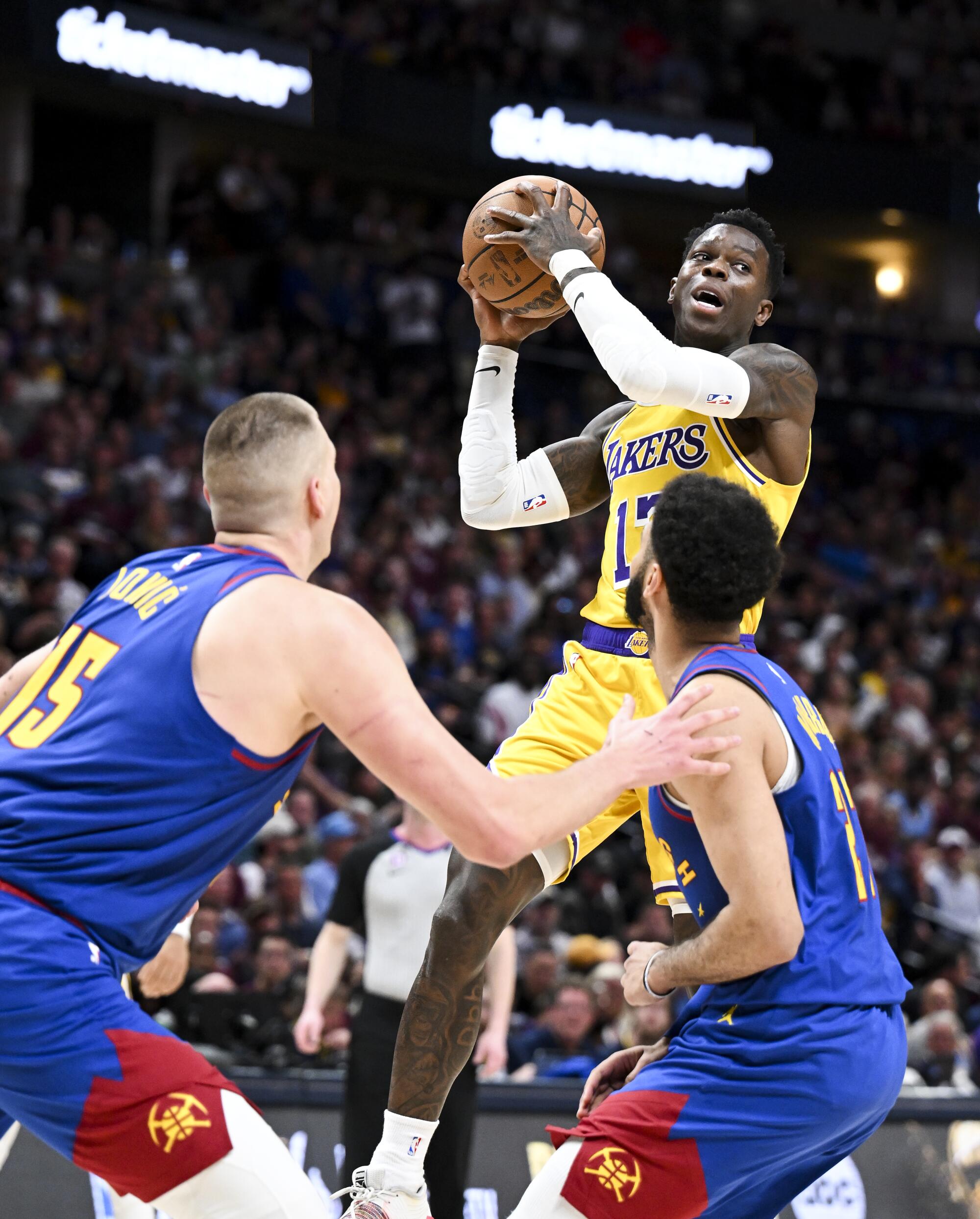 Lakers guard Dennis Schroder looks pass the ball while Nuggets guard Jamal Murray and center Nikola Jokic defend.