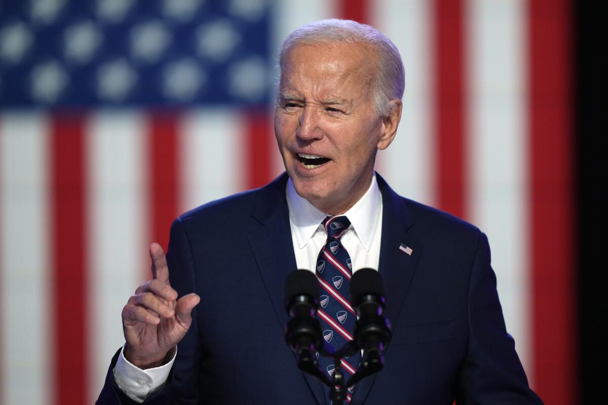 President Biden gestures while speaking before a large U.S. flag