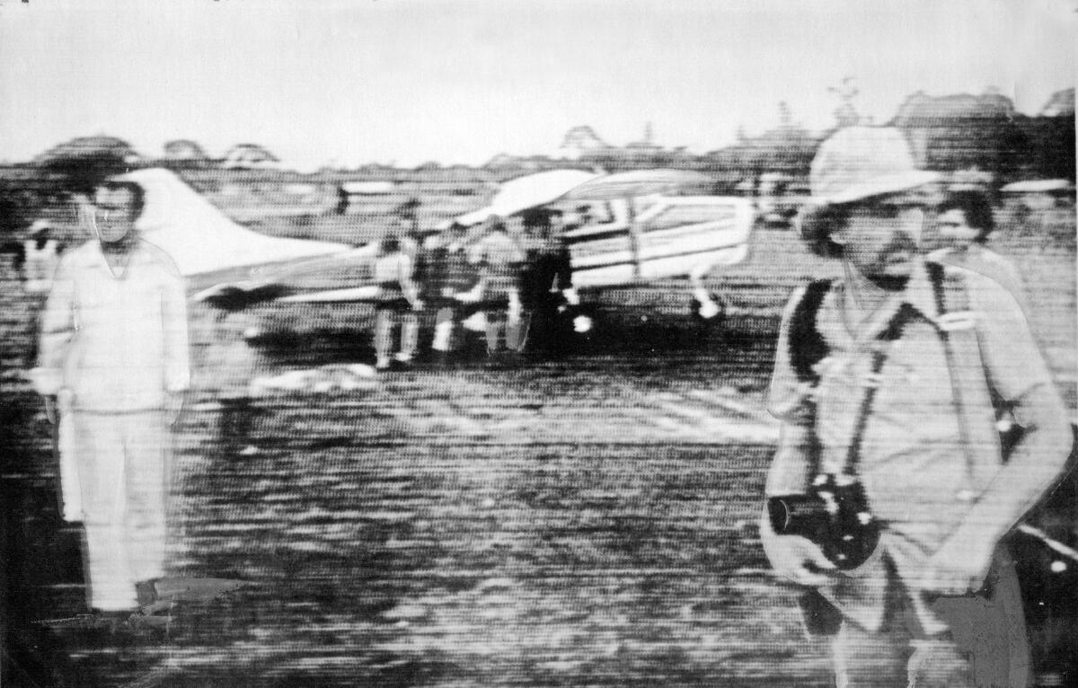 A black-and-white photograph of a journalist and photographer in front of a small plane.