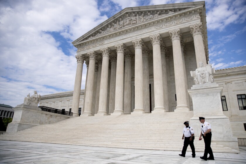Security officers, one wearing a mask, walk on the sidewalk in front of the Supreme Court building in Washington