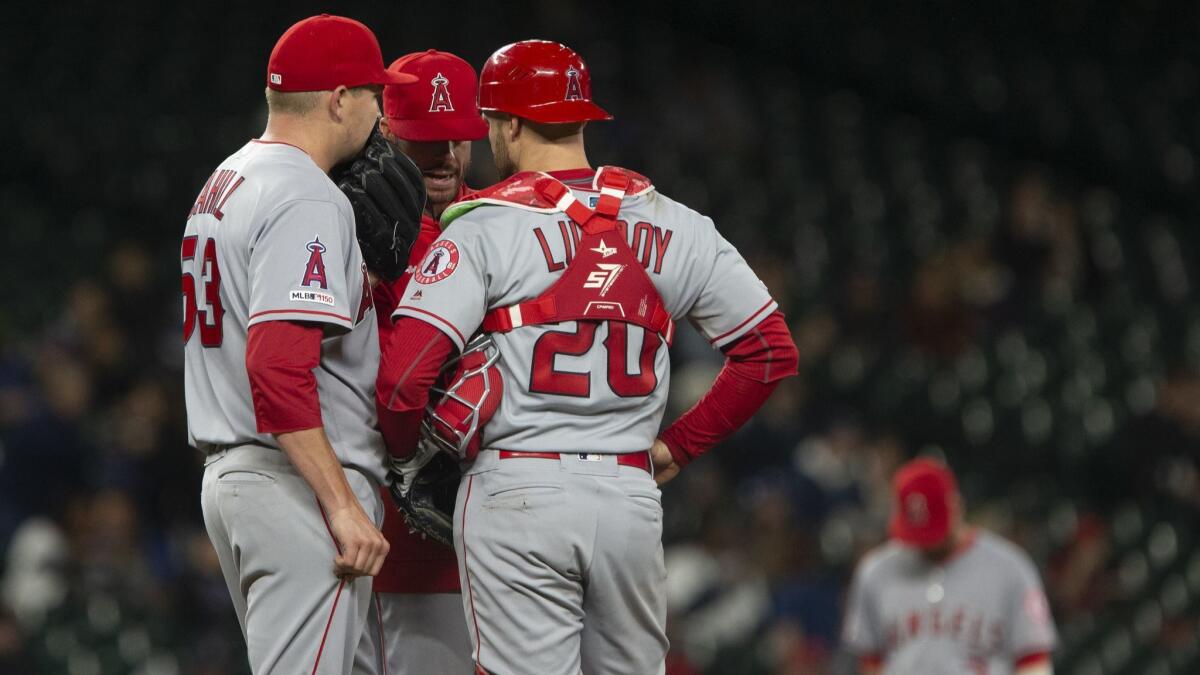 Angels' Trevor Cahill (53) and Jonathan Lucroy (20) huddle with pitching coach Doug White in the sixth inning against the Seattle Mariners on Tuesday in Seattle.