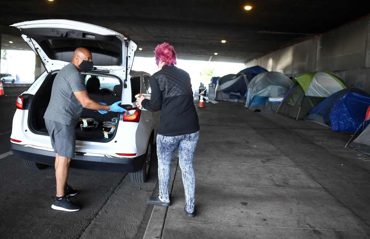 Tom Crump hands out free lunch to a homeless woman on Venice Boulevard under the 405 Freeway in Los Angeles on Tuesday.