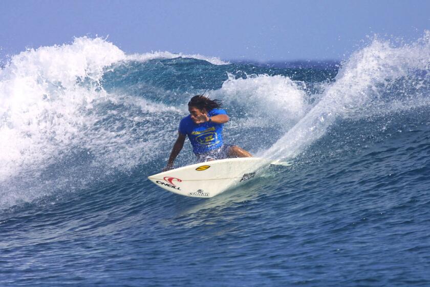 Tamayo Perry wearing a blue rash guard and surfing in Tahiti