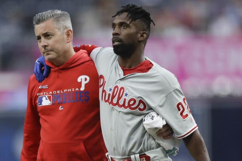 Philadelphia Phillies' Andrew McCutchen, center, is helped by a trainer after being injured trying to get back to first base during the first inning of a baseball game against the San Diego Padres Monday, June 3, 2019, in San Diego. (AP Photo/Gregory Bull)