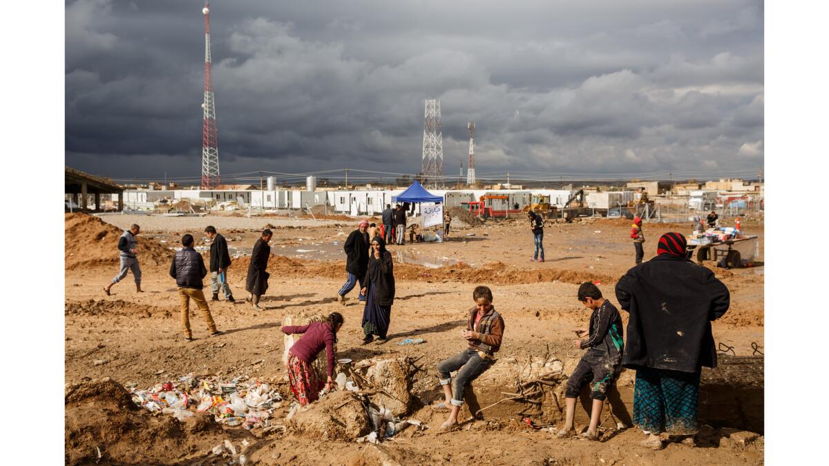 People linger outside during a pause in the rain at a U.N. displaced persons camp in Hamam Alil, Iraq.