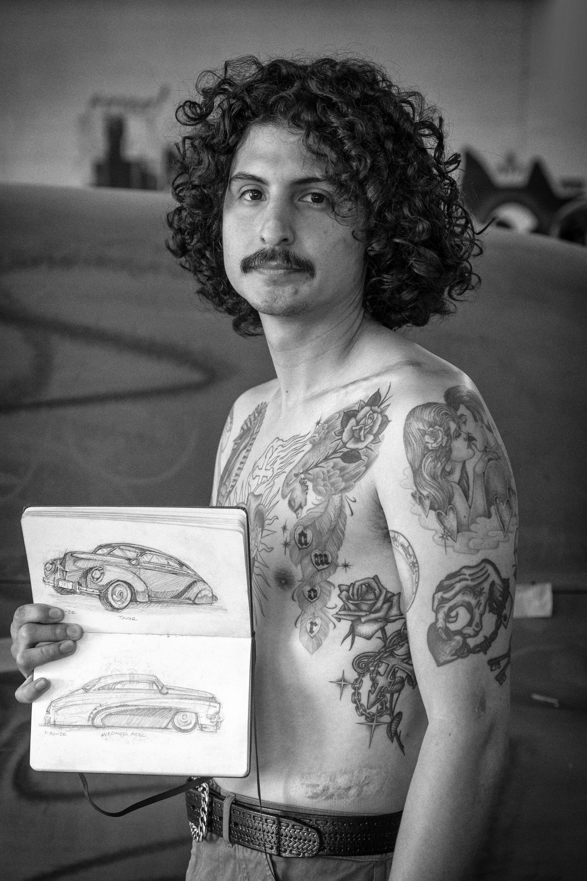 a black and white photo of Jesse Jaramillo holding up a note book with sketches of a classic car