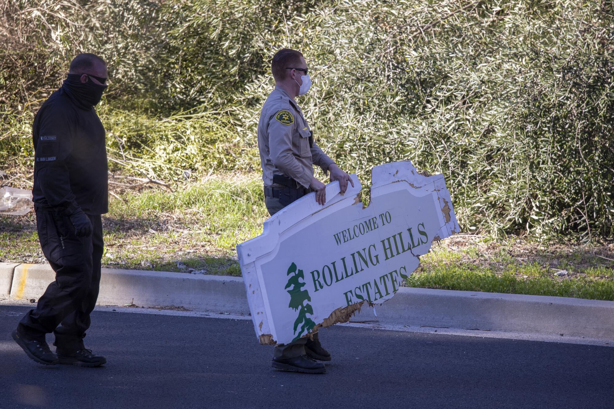 L.A. County Sheriff deputy picks up a damaged sign that reads "Welcome to Rolling Hills Estates" from the scene 
