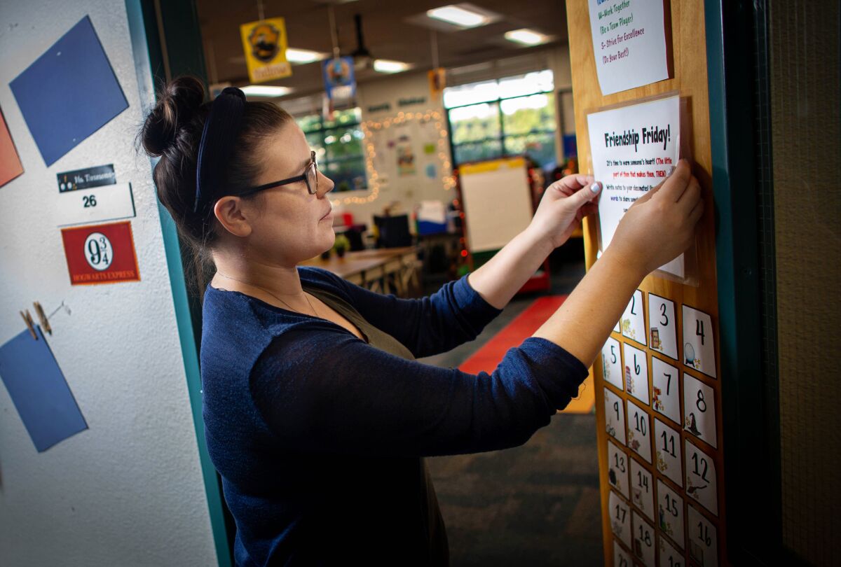 A teacher puts a laminated sign that says Friendship Friday on her classroom door