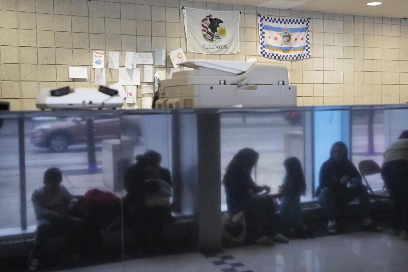 FILE - Immigrants from Venezuela are reflected in a marble wall while taking shelter at the Chicago Police Department's 16th District station on May 1, 2023. Chicago officials have signed a nearly $30 million contract with a private security firm to relocate migrants seeking asylum from police stations and the city’s two airports to winterized camps with massive tents before cold weather arrives. (AP Photo/Charles Rex Arbogast, FIle)