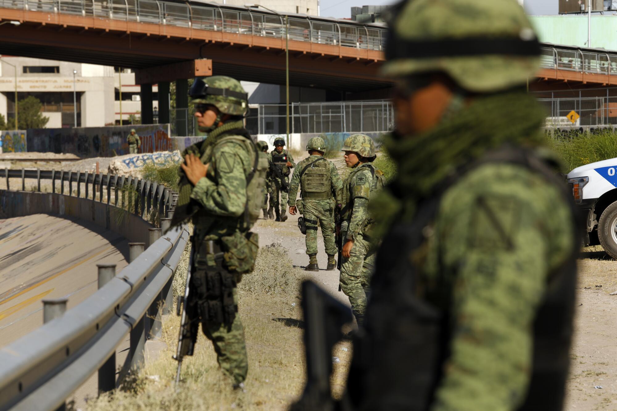 Members of the Mexican National Guard stand between a roadway and wall. 