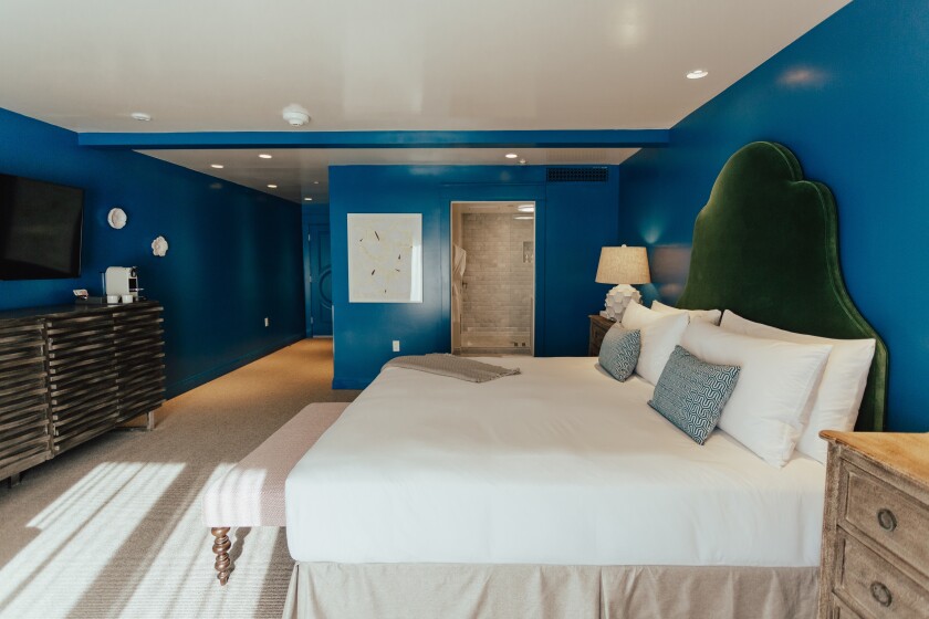 A hotel room with deep blue walls and a white bed