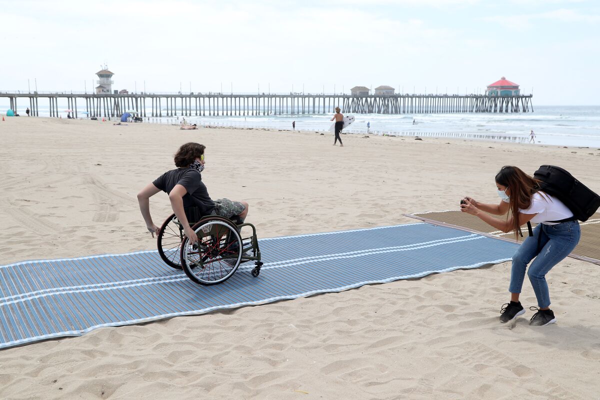 Adaptive surfer Kumaka Jensen, 14, rolls out on the first Mobi-Mat in Huntington Beach during a ceremony on Wednesday.