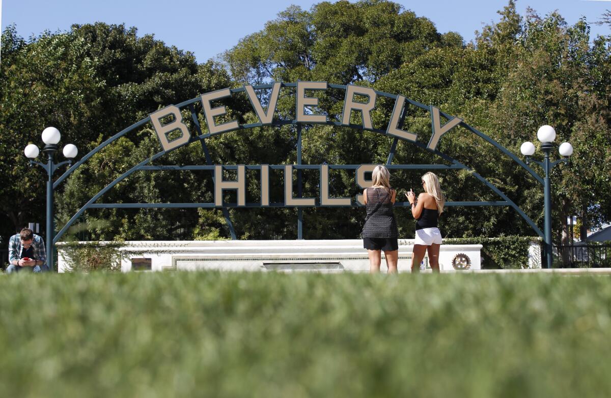 Two women stand in front of a Beverly Hills sign in a park