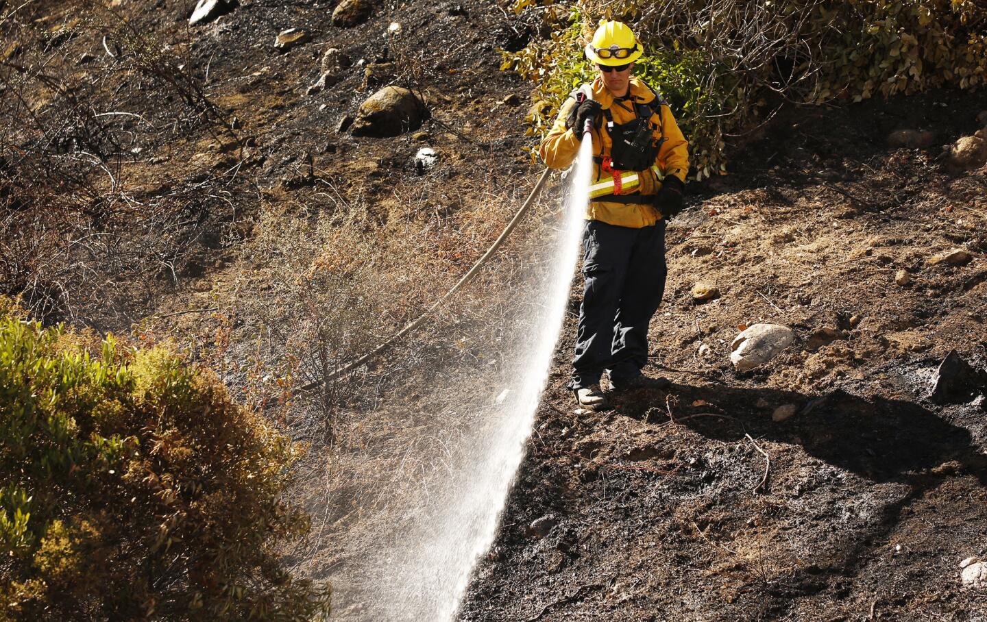 As temperatures begin to climb, Nick Spurlock with the Orange County Fire Authority waters embers on burned hills in the Placerita Canyon area of Santa Clarita.