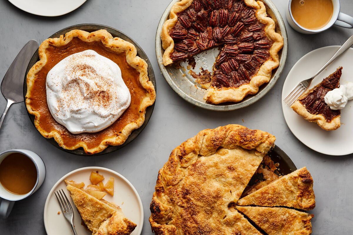 A variety of Thanksgiving pies are displayed on a table, some with slices removed.