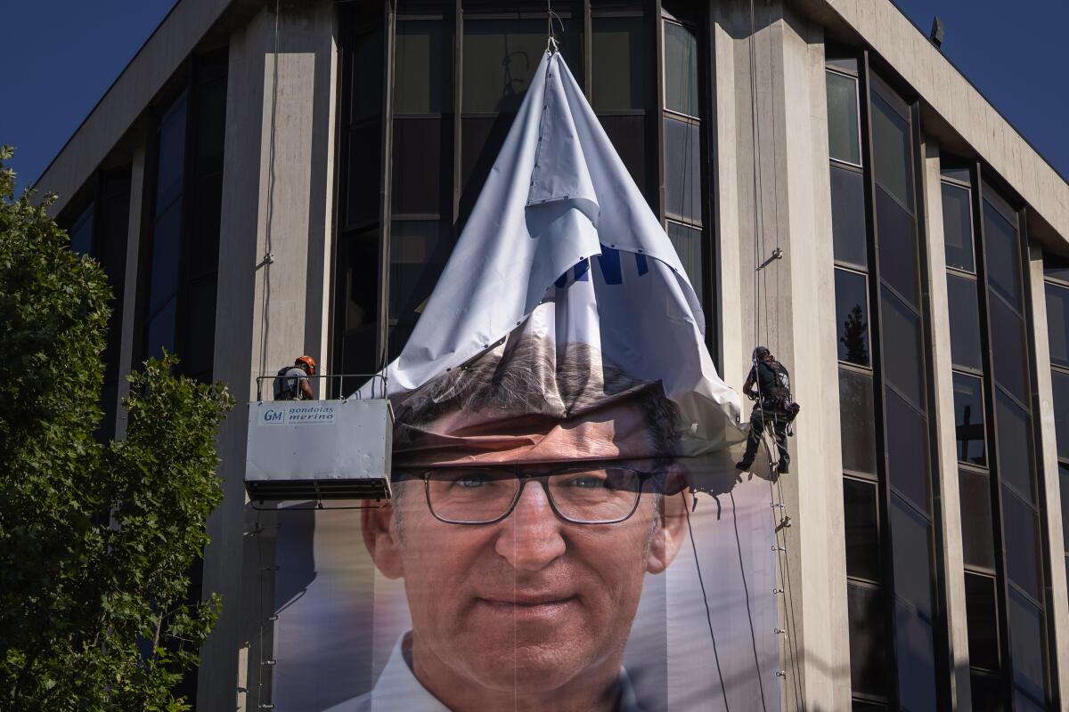 Workers remove an electoral poster, showing a man's face, from the side of a building.