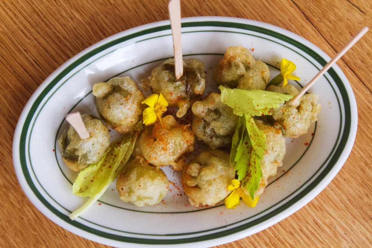 An overhead photo of a small plate of merguez-stuffed fried olives garnished with celery leaves and yellow flowers
