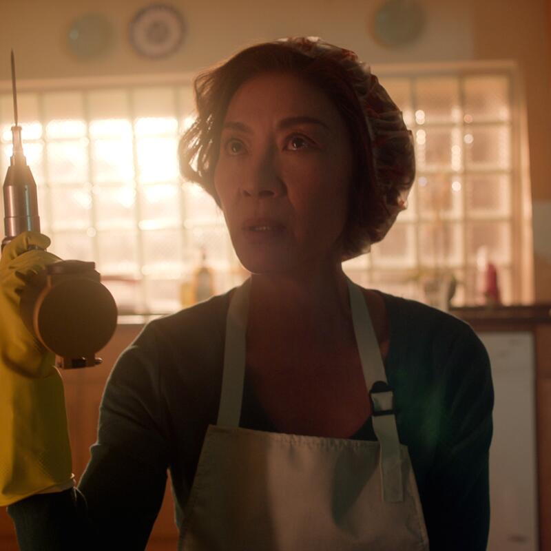 A woman wearing yellow rubber gloves and an apron holds up an electric saw.