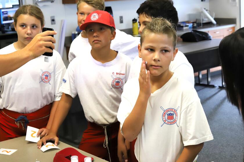 Ryder Maragos, 10, right, and with other Huntington Beach Junior Lifeguards are shown how to correctly apply sunscreen.