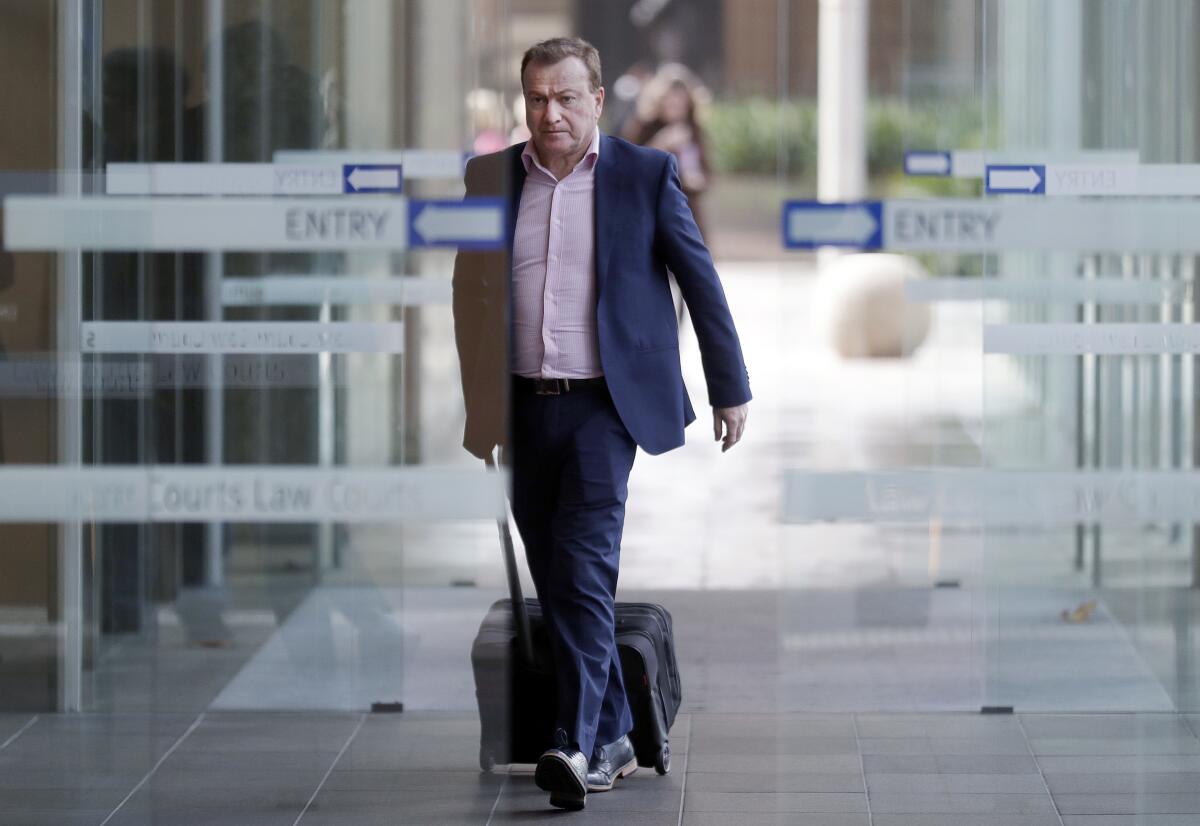 A man in a suit jacket pulls a rolling briefcase as he passes through glass doors.