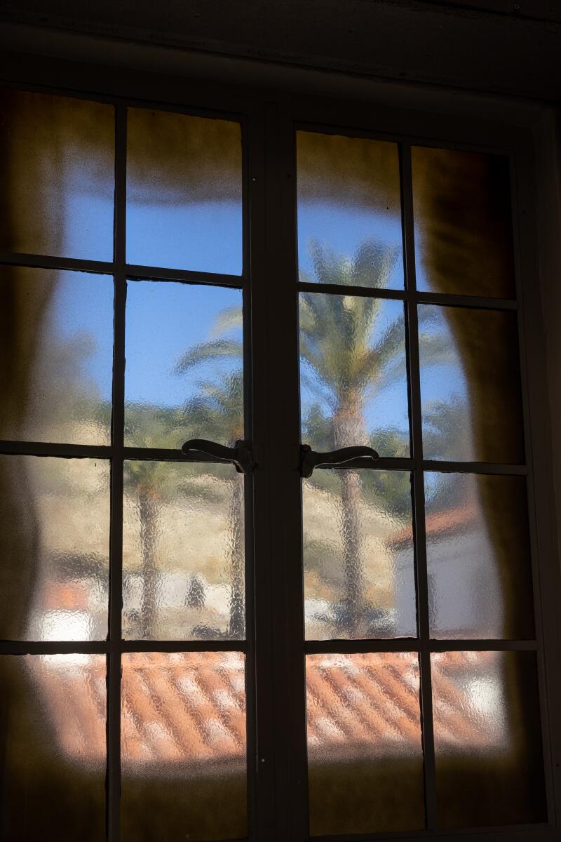 The view through a patterned glass window looks onto red tiles roofs and palm trees