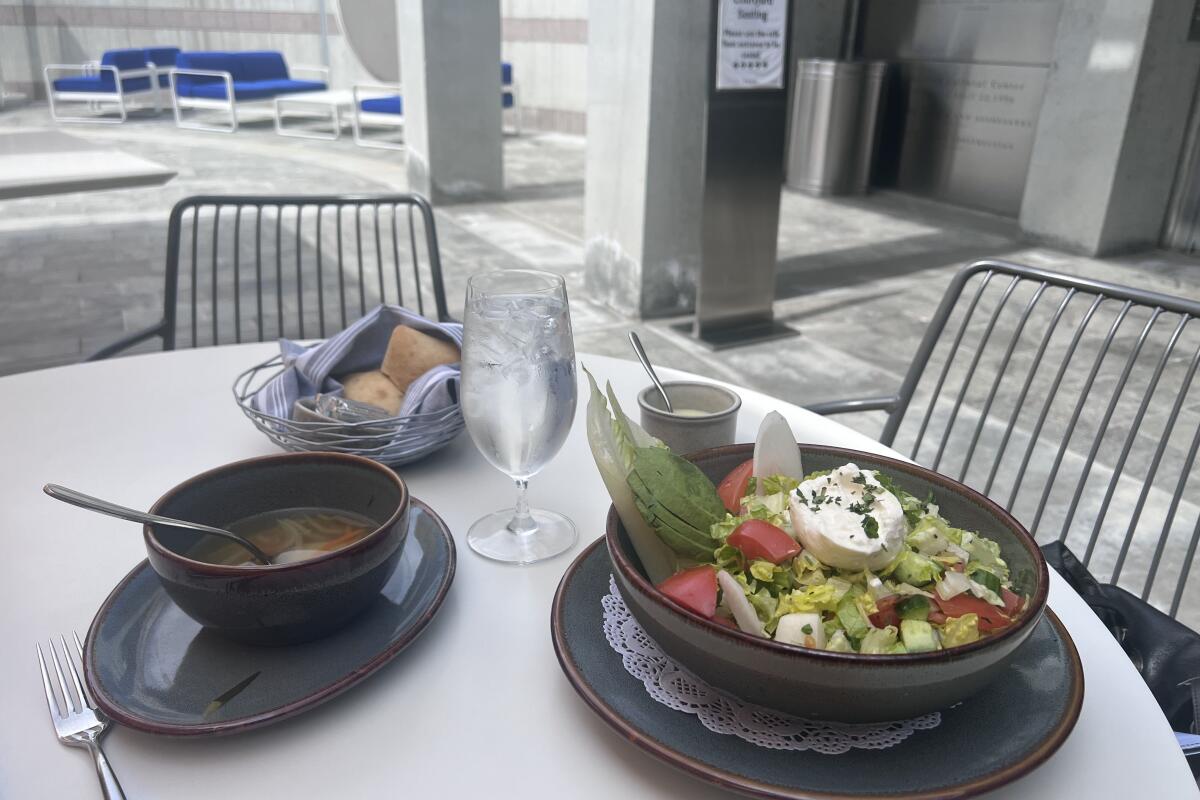 Matzo ball soup, bread and butter and an Israeli chopped salad on a table in a courtyard