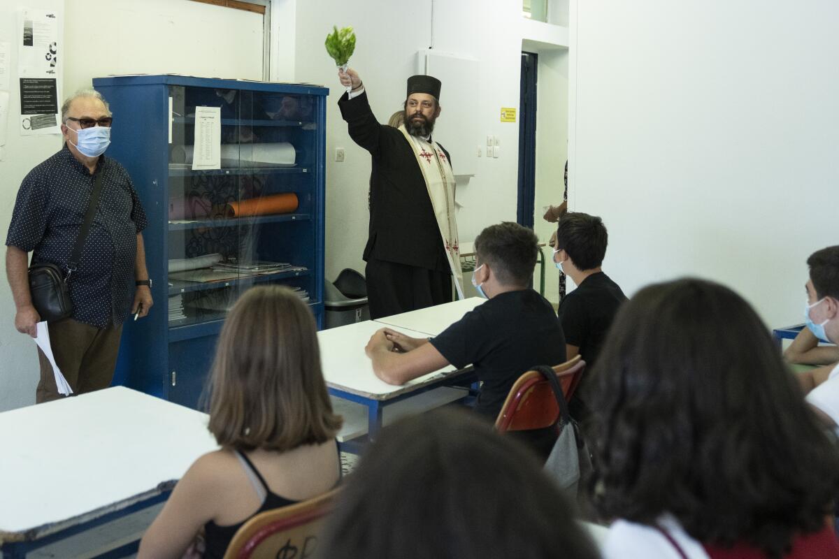 A Greek Orthodox priest blesses students in a classroom of a junior high school in Athens, Monday, Sept. 13, 2021. Public and private sector employees will have to pay for weekly tests or carry a vaccination certificate to gain access to their place of work, while unvaccinated children at high schools which reopened Monday are being given test kits distributed at the government's expense. (AP Photo/Petros Giannakouris)
