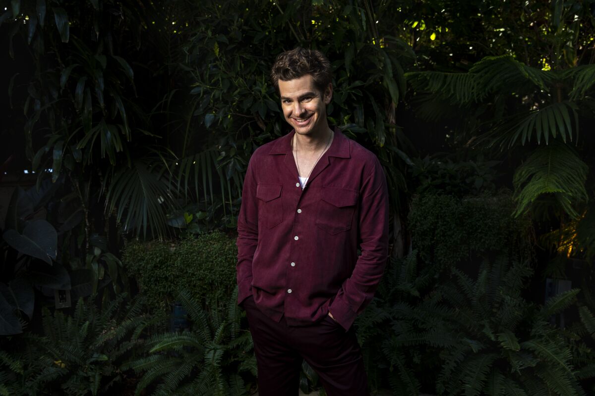 A man in a maroon shirt smiles in front of foliage