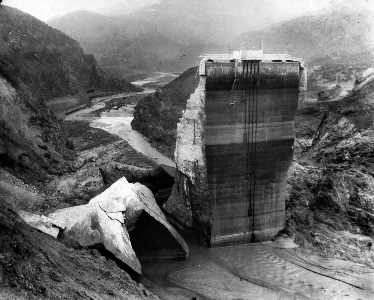 A portion of a concrete dam stands in a river valley with crumbled pieces surrounding it