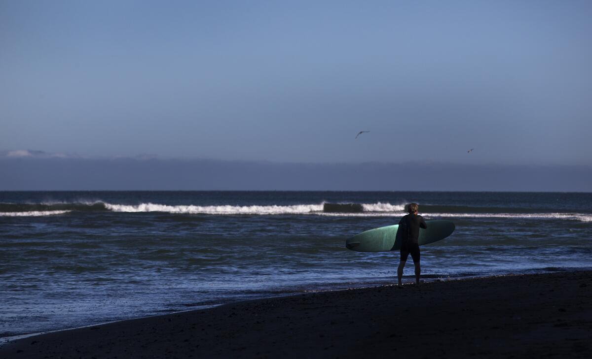 A surfer passes through a ray of the setting sun in Bolinas Bay.