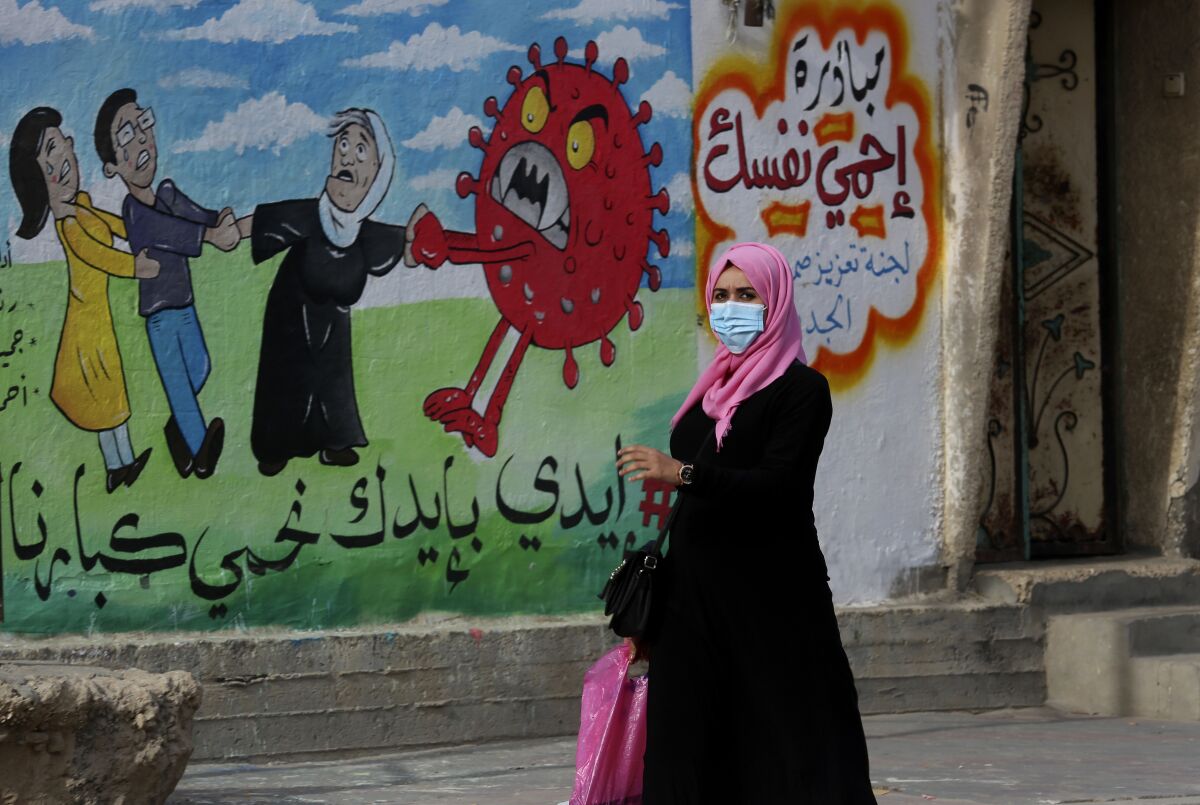 FILE - A woman walks past a mural encouraging the wearing of face masks amid the coronavirus pandemic, on the main road of Nusseirat refugee camp, central Gaza Strip, on Nov. 24, 2020. Arabic reads: "protect yourself, together we protect the old." The prickly orb is on every news and medical site. It's all over TV and on flyers for COVID car cleaning. (AP Photo/Adel Hana, File)