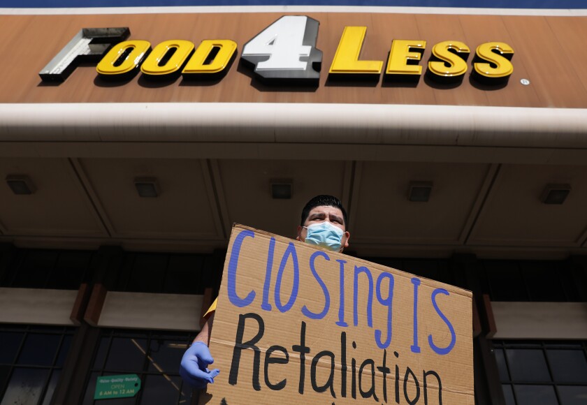Protester holds a sign saying "closing is retaliation" in front of a grocery store. 