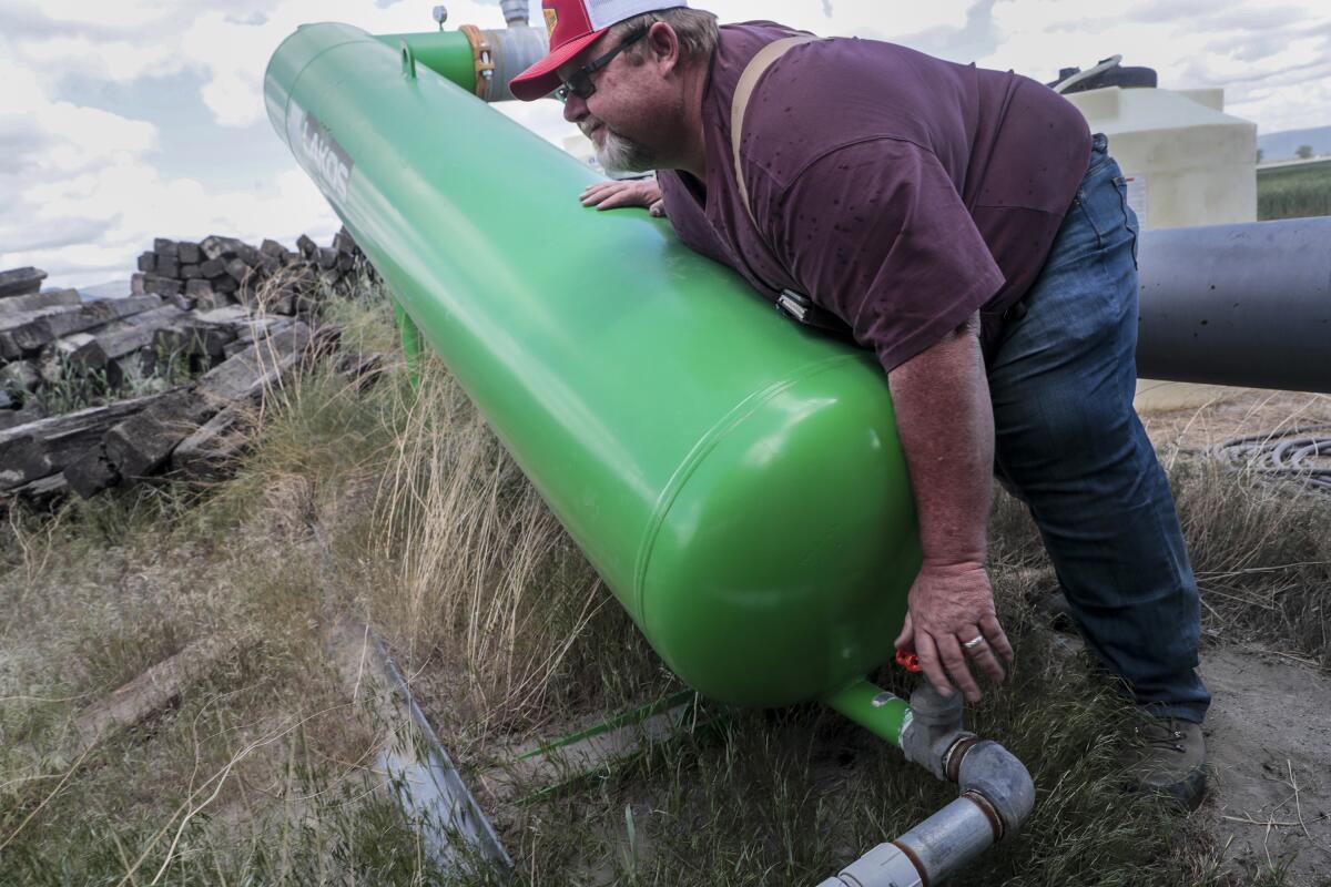 A farmer opens a valve on a green tank