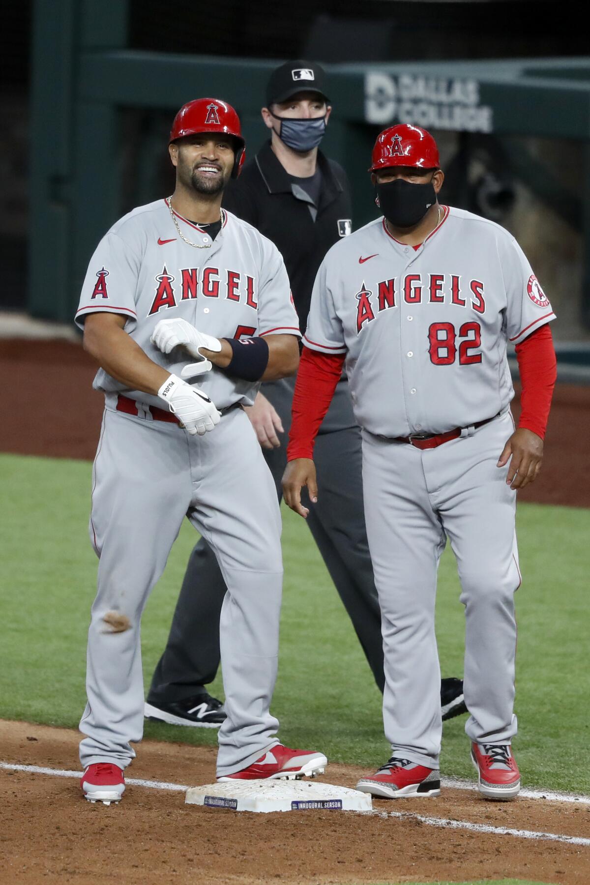 Angels' Albert Pujols stands by first-base coach Jose Molina smiling.